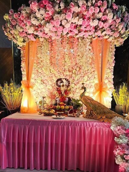 For a truly royal feel, I created this stunning Ganpati mandap with a ceiling completely covered in pink and white flowers. The backdrop is a wall of white flowers, with peach drapes and a beautiful peacock figurine adding to the grandeur.