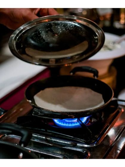 A chef prepares a fresh appam in a special pan over a live flame. This showcases our ability to execute specialized regional dishes that require specific techniques and equipment.