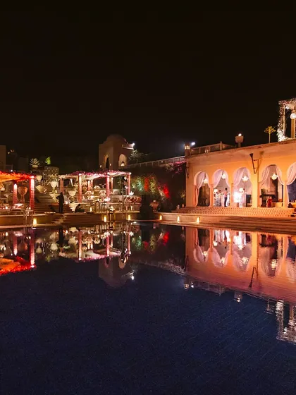 A stunning view of a poolside wedding setup at the Oberoi Amarvilas in Agra. The reflection of the beautifully lit mandaps and decor in the water creates a scene of pure charm and elegance.