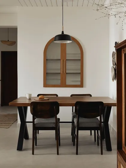 In this open-plan home, I used a grooved ceiling to visually define the dining area. The dark wood table and chairs create a sense of intimacy, while the arched crockery cabinet on the wall adds a touch of Japandi-inspired elegance.