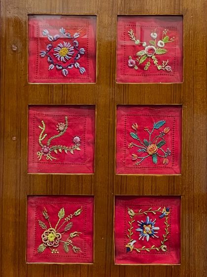 A set of six framed floral embroidery pieces on a vibrant red background. These are available for purchase and would brighten any room.