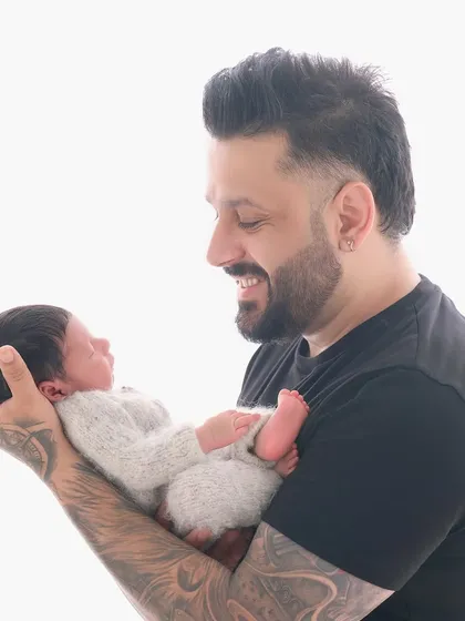 A proud father with tattooed arms gently holds his newborn baby. This image beautifully contrasts strength and tenderness, captured with our bright and airy studio lighting.