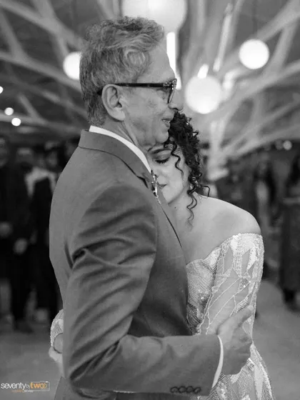 A tender black and white photo of a bride dancing with her father, her head resting on his shoulder in a moment of love and gratitude.