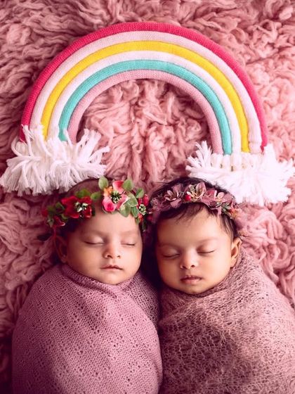Sometimes, the simplest setups are the sweetest. Here are two twin sisters swaddled in soft pink wraps, with floral crowns and a rainbow to celebrate their arrival.