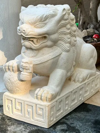 A side profile of the male Foo Lion statue, shown resting its paw on a ball. The sandstone material gives it a classic, timeless look suitable for both modern and traditional homes.
