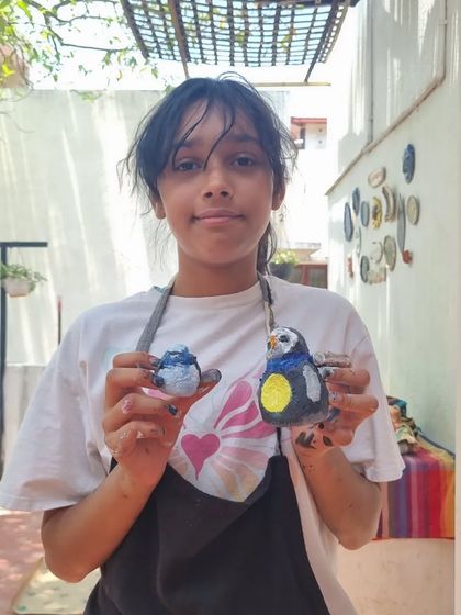 A young artist proudly displays the clay birds she made and painted during our kids' workshop. We encourage children to explore form and color.