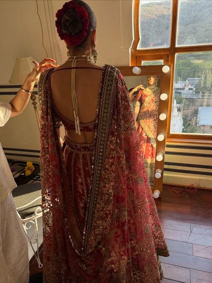 A behind the scenes glimpse as the bride gets her final touches. You can see how the makeup beautifully complements the low bun adorned with red roses and the stunning back detail of her blouse.