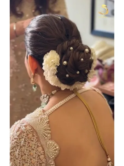 A close-up of a textured bridal bun, intricately woven and decorated with white flowers and delicate pearls.