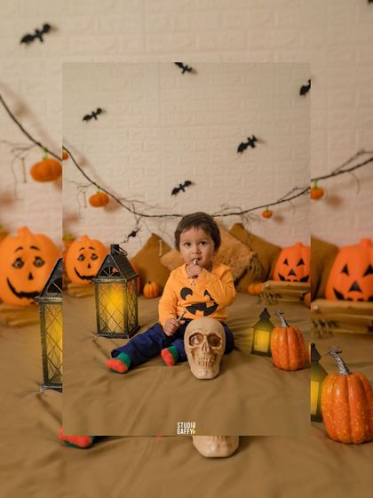 A cute baby in a pumpkin-themed shirt surrounded by spooky Halloween decorations.