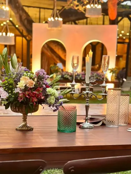 A close-up of the tablescape, featuring elegant floral centerpieces, classic candle holders, and high-quality glassware. The warm wood of the table complements the natural surroundings.