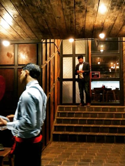 An interior view of a commercial project, showcasing a rustic aesthetic with reclaimed wood on the walls and ceiling, exposed bulbs, and a multi-level layout defined by a short staircase.