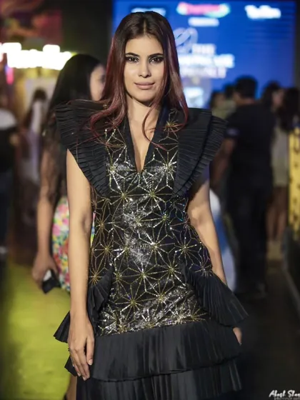A model in a black and gold geometric-patterned dress with pleated details, captured mid-walk at 'The Showcase Project'.
