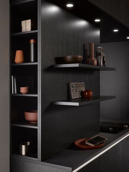 Detail of the open shelving in the black oak wickerwork kitchen. The dark interior and subtle lighting create a moody and sophisticated display area.
