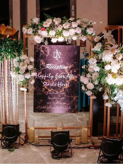 "Happily Ever After Starts Here." We designed this modern reception welcome sign with a marble-effect background, framed by white florals and glowing candles.