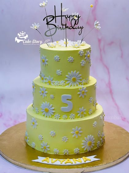 A cheerful three-tier cake covered in fondant daisies. The bright yellow color and simple floral design make it a sunny and happy centerpiece for a 5th birthday.