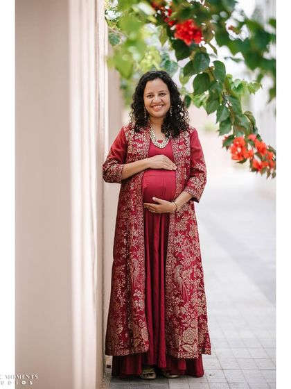 A full-length solo portrait of the mother-to-be in a gorgeous red embroidered outfit. The vibrant flowers in the background complement her attire perfectly.