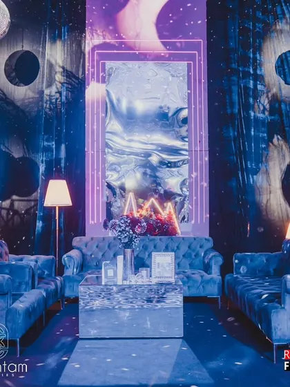 A cozy lounge setup from the retro disco sangeet. The seating area features plush blue velvet sofas, a mirrored coffee table, and a backdrop of abstract, cosmic-themed panels with neon-framed mirrors, creating a stylish and comfortable space for guests.