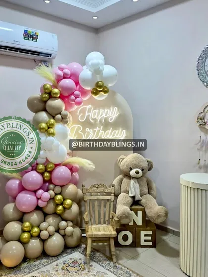 A cozy and cute teddy bear-themed first birthday. The balloon garland in nude, pink, and white, paired with a neon sign and a fluffy teddy bear, creates a warm and inviting corner.