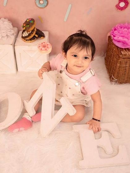 Exploring the props before the donut smash begins. This little one is checking out the "ONE" letters in our sweet, pink-themed donut setup.