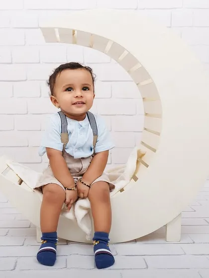 A simple and sweet portrait of a one-year-old boy sitting on a white crescent moon prop against a brick wall backdrop.