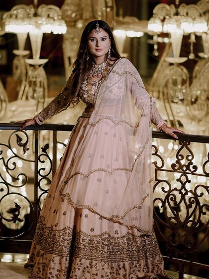 A stunning bridal portrait from an engagement ceremony. The grand chandeliers in the background add a touch of luxury, perfectly matching the bride's elegant pastel lehenga.