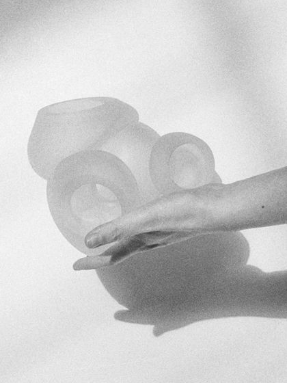 A black and white photo showing a hand interacting with the delicate, frosted glass of the Bocci 100 series, emphasizing its tactile quality.