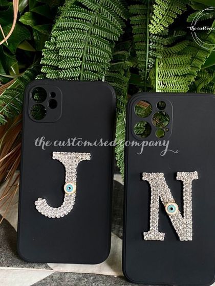 Protect your phone in style. These black phone cases are customized with a large, sparkling rhinestone initial that also incorporates a subtle evil eye for protection.
