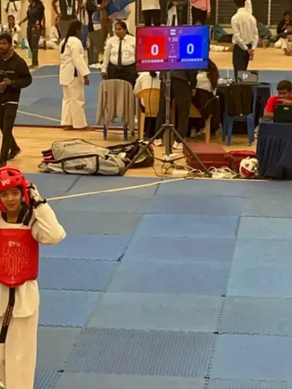 A student gets ready for her Kyorugi (sparring) match, wearing her protective gear and looking determined. The scoreboard is ready for action.