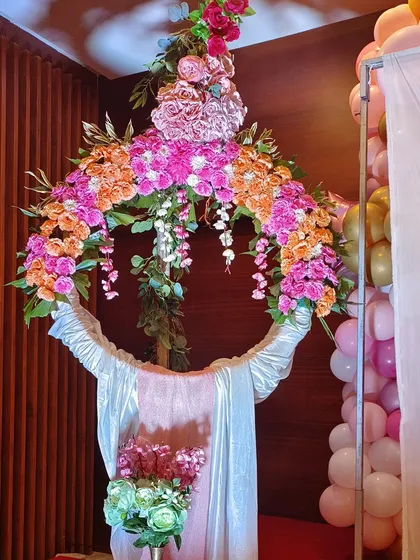 This modern floral hoop is a unique and stylish alternative to a traditional backdrop for a naming ceremony. The ring is decorated with a lush arrangement of pink and orange flowers, creating a vibrant focal point.