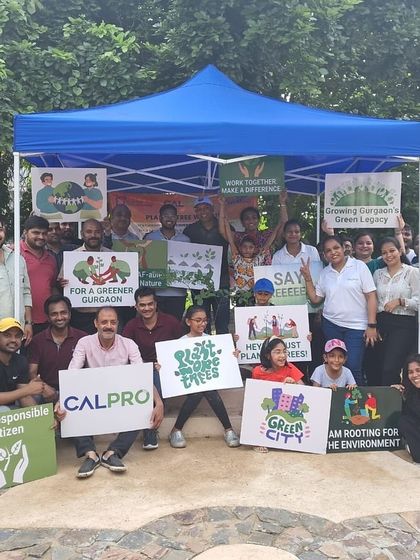 The full team from Calpro Specialties, including children, poses with signs celebrating their contribution to a greener Gurgaon at Aravali Creek.