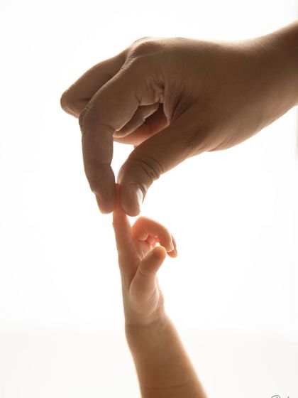 The delicate touch between a parent's hand and their baby's tiny fingers. This backlit, artistic shot highlights the beautiful, fleeting details of the newborn stage.
