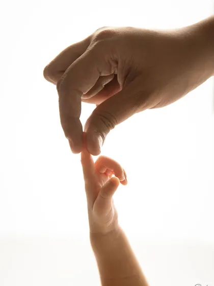 The delicate touch between a parent's hand and their baby's tiny fingers. This backlit, artistic shot highlights the beautiful, fleeting details of the newborn stage.