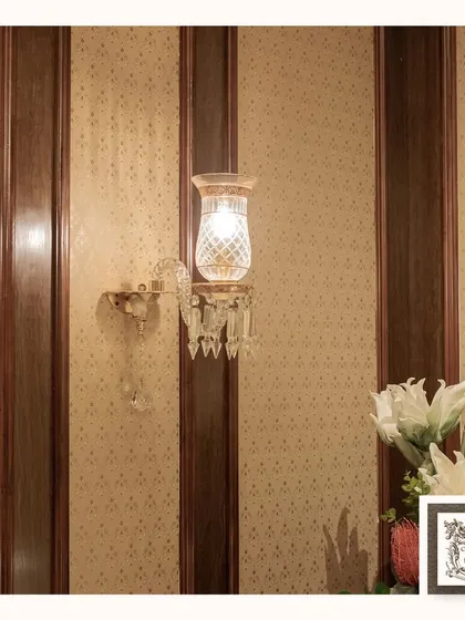 This artisan-crafted wall sconce is a testament to detailed craftsmanship. Featuring a delicate glass shade, crystal drops, and a classic brass fixture, it provides a soft, ambient glow ideal for hallways, studies, or any space needing a touch of royal elegance.