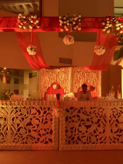 A beautifully carved bar counter with intricate details, illuminated from within. The red and gold draping above adds a touch of traditional luxury.