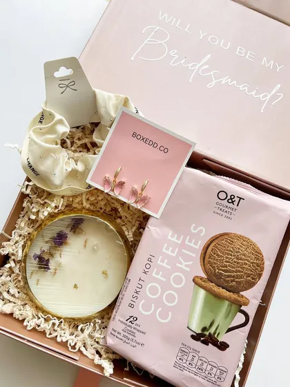 A simple yet sweet bridesmaid proposal box with coffee cookies, a scented candle, and a scrunchie, asking the important question right on the lid.