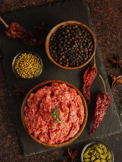 A clean, top-down shot of minced meat and spices on a dark slate. This minimalist flat lay is both artistic and informative, clearly showing the key ingredients for a flavorful dish.