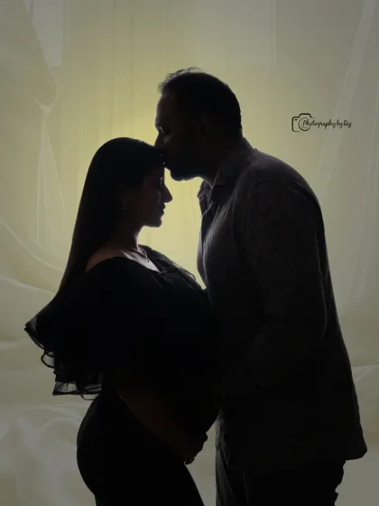 A tender silhouette of a couple, with the father-to-be kissing the mother-to-be's forehead.