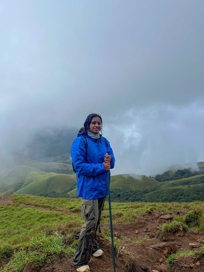 A trekker with her hiking pole stands against the misty green hills of Kudremukha, fully prepared for the trail.