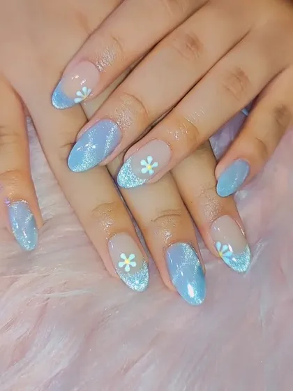 A dreamy, sky-blue glitter polish with a French-style tip. Accent nails are adorned with tiny, hand-painted white daisies for a sweet, summery vibe.