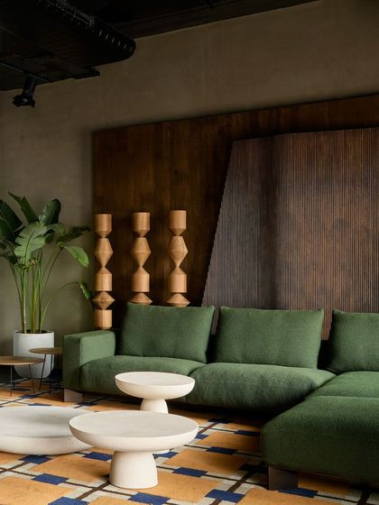 A closer look at the green sectional sofa and sculptural wooden totems. The exposed ceiling with track lighting gives the retail space an industrial edge, which contrasts with the warm, residential feel of the furniture.