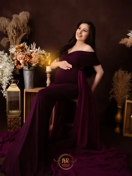 A classic seated portrait in a deep plum-colored gown. The rustic, candlelit setting adds a warm and timeless feel to this elegant pregnancy photo.