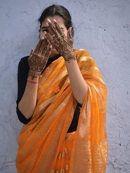 A client in a beautiful saree, hiding playfully behind her hands, which are adorned with a lovely, mature henna stain.