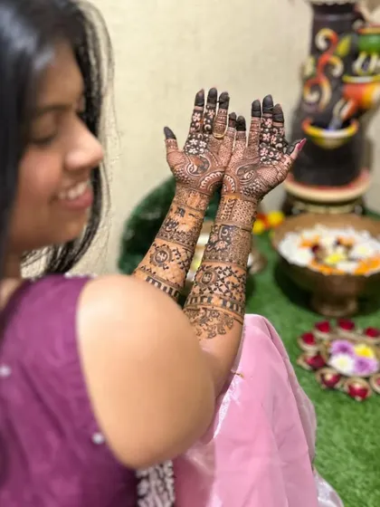 A candid shot of a bride-to-be admiring her intricate mehendi. The design features detailed work on both the front and back of her hands.