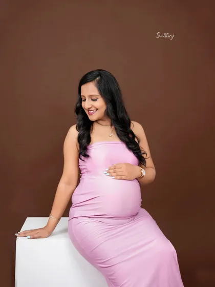 A simple and elegant portrait of a mother-to-be in a lavender gown. The solid brown background provides a beautiful contrast, making her the center of attention.