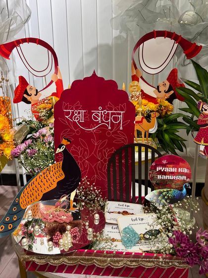A peacock-themed Rakhi platter. The large red cutout with "Raksha Bandhan" in Hindi and the peacock motif make it a very grand and traditional gift.