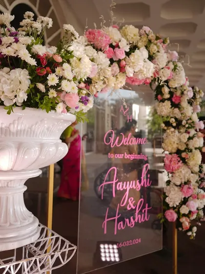 A close-up of this acrylic welcome sign, where the bright pink calligraphy stands out against the lush floral arch, creating a modern and vibrant look.