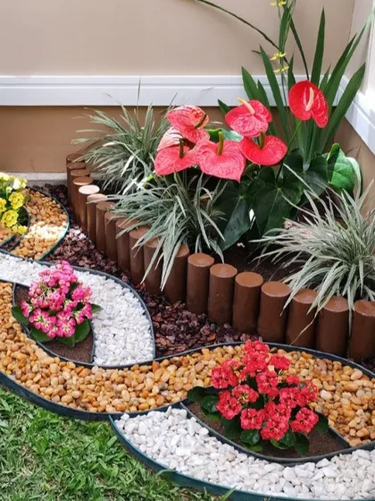 We love adding artistic touches to our gardens. This corner showcases a creative pebble art design using contrasting colors of natural and white stones to create flowing, leaf-like patterns. The design is complemented by colorful flowering plants and a natural wood log border, turning a simple corner into a beautiful focal point.
