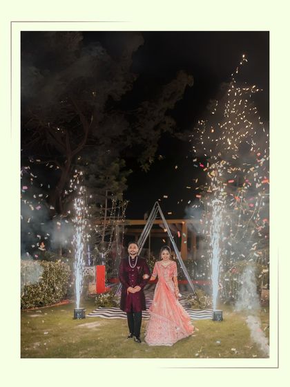 Alankrit and Parul make a grand entrance at their ring ceremony, framed by sparklers. This wide shot captures the celebratory atmosphere of the night.