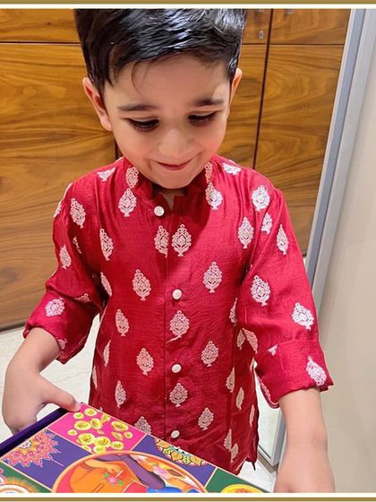 A sweet moment captured with a festive gift. Our little client looks charming in his red printed kurta, ready to celebrate with his family.