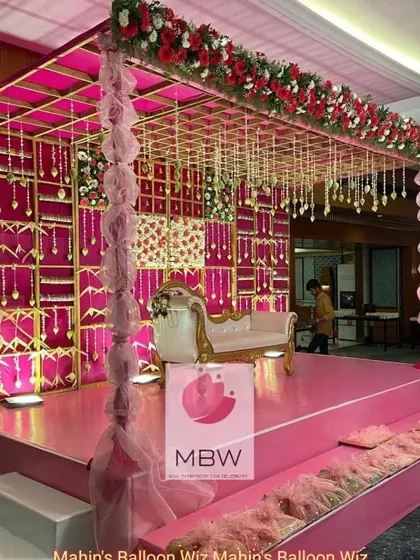 An opulent stage setup perfect for a wedding reception or anniversary. The design features a rich pink and gold color scheme, with a decorative backdrop, elegant draping, and crystal hangings.